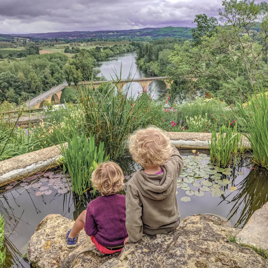 two boys sat on rock looking over a river